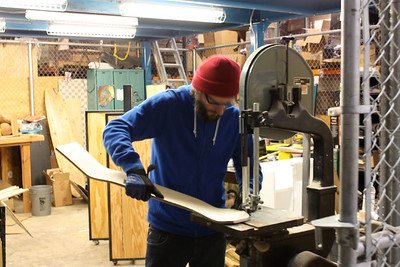 A man cutting a piece of wood in his work station