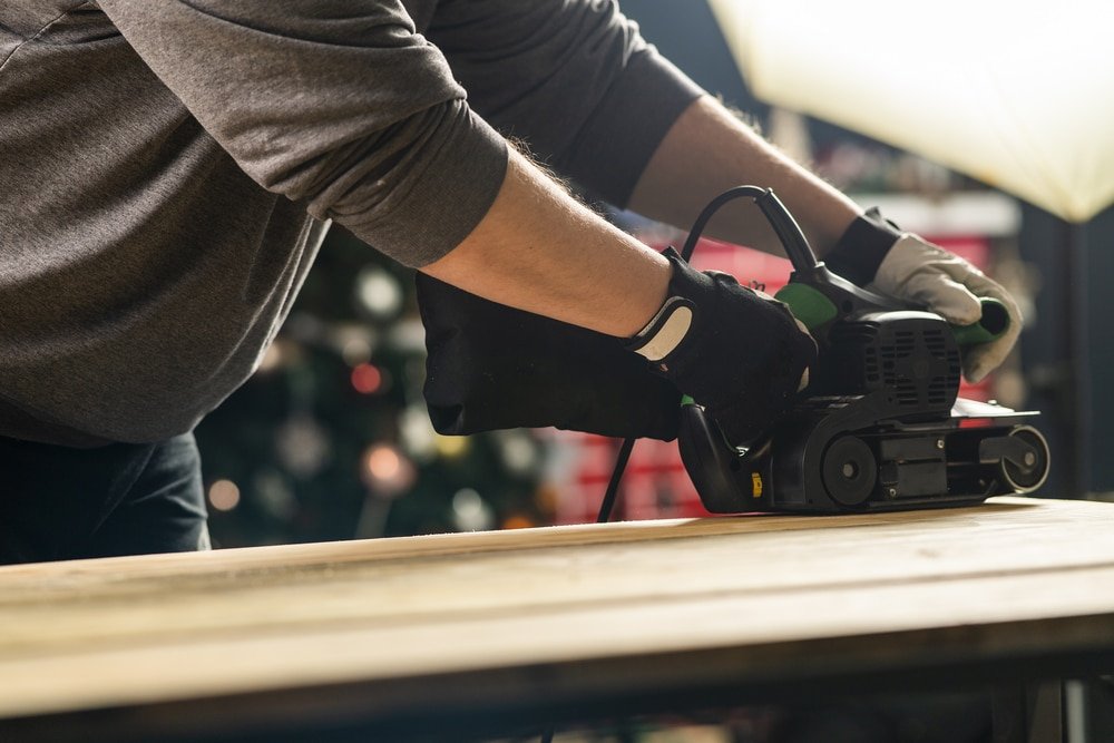A man sanding a piece of wood using an electric tool.
